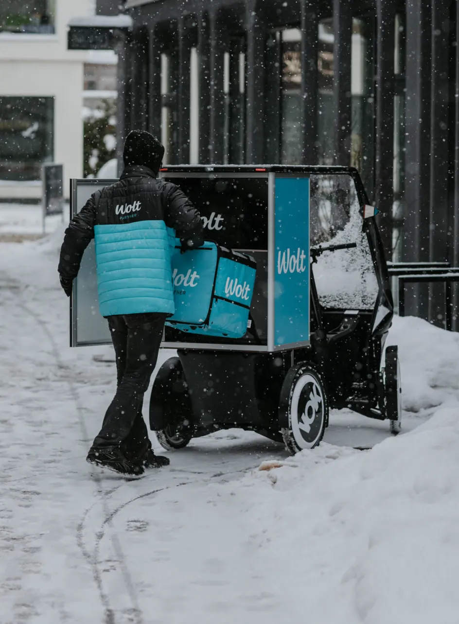 Kurier Wolt ładuje torby z jedzeniem do roweru cargo VOK podczas opadów śniegu